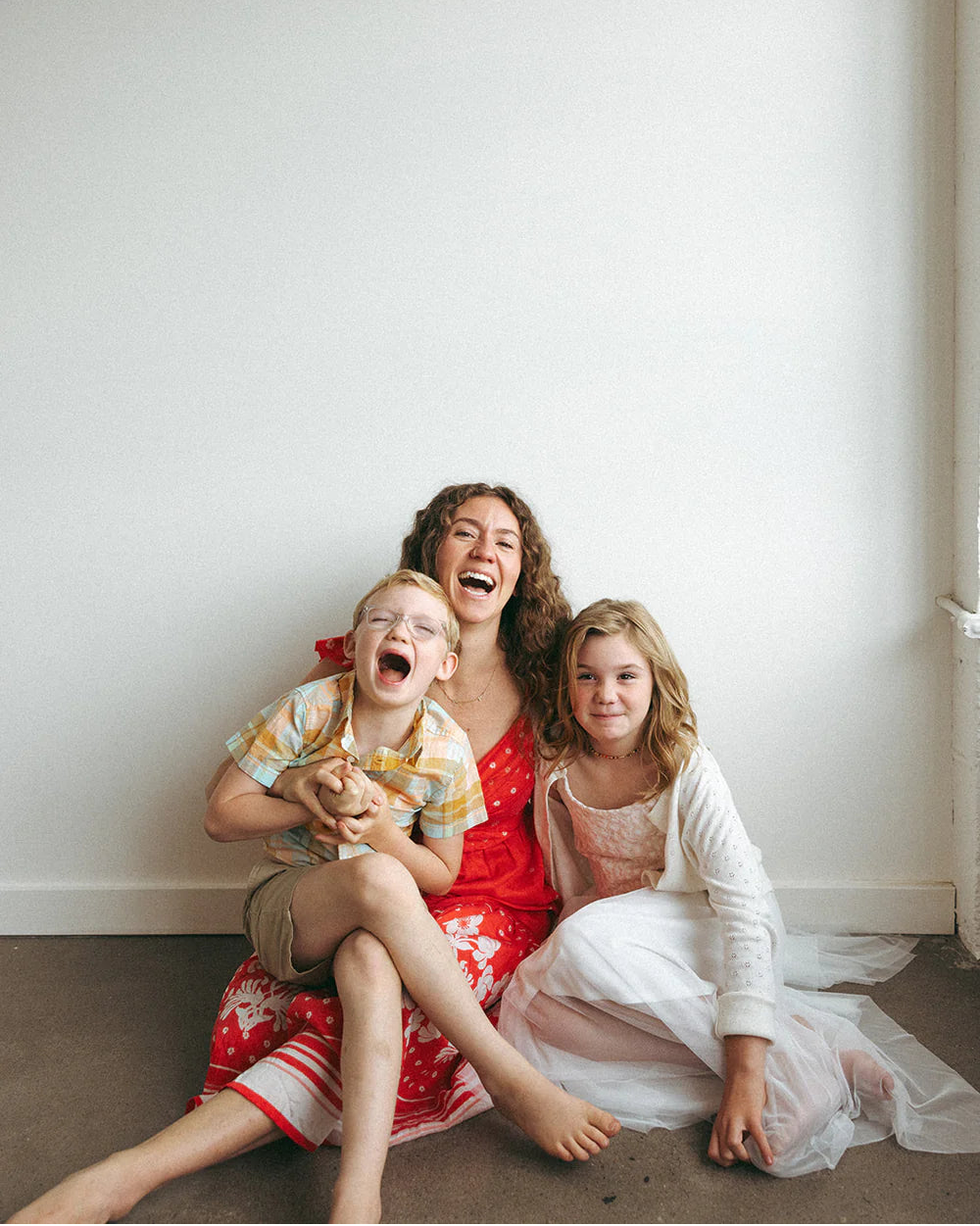 Woman and two children sitting on the floor against a white wall